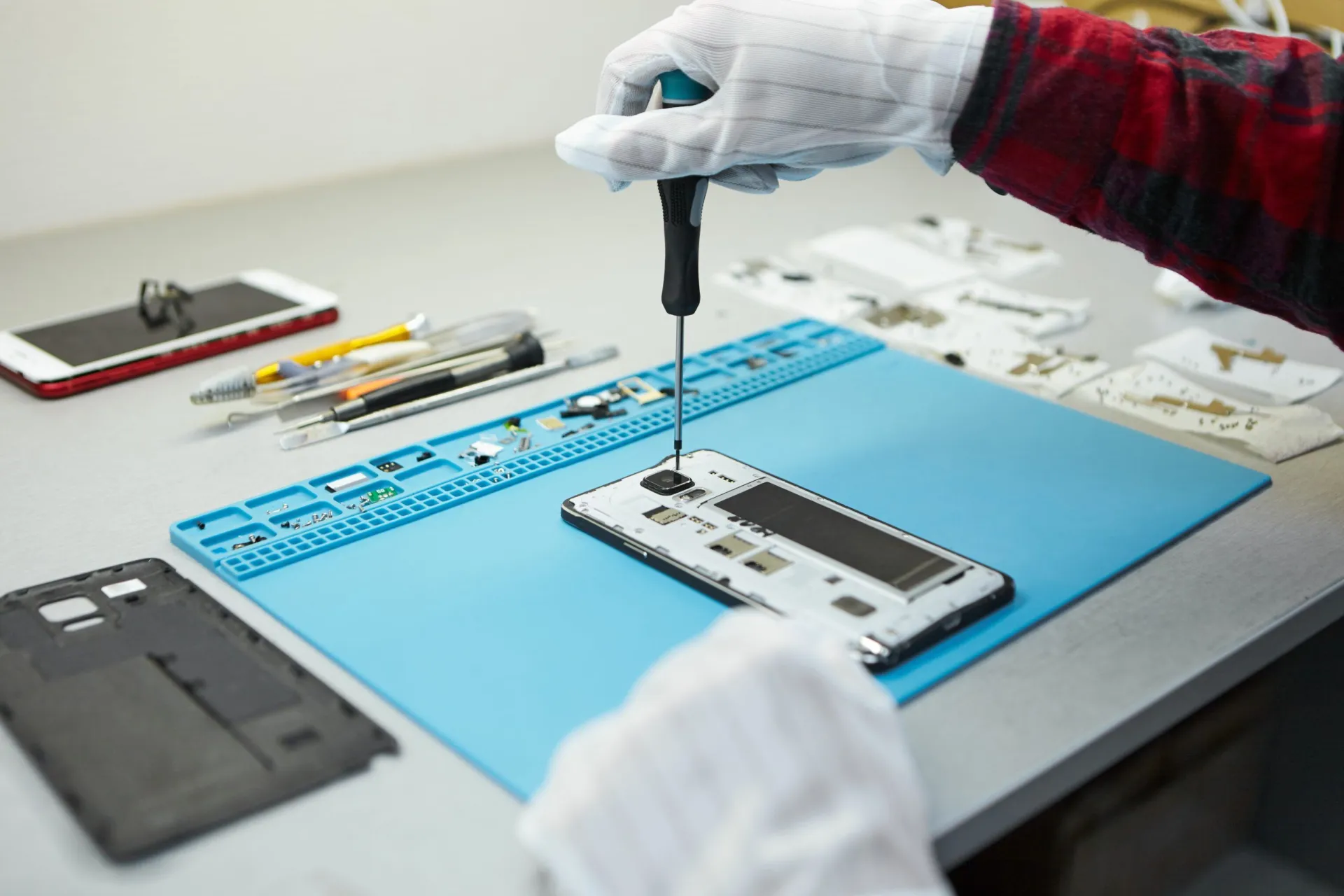 technician-in-antistatic-gloves-using-screwdriver-to-disassemble-borken-mobile-phone-going-to-repair-motherboard-sitting-at-his-workplace-in-laboratory-with-needed-equipment-scaled.jpg