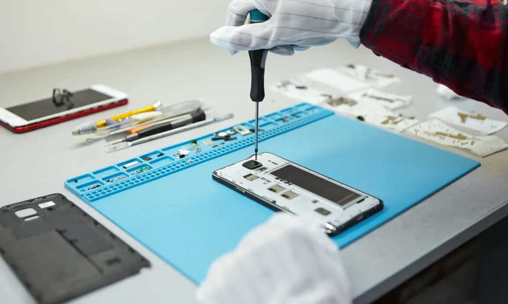 technician-in-antistatic-gloves-using-screwdriver-to-disassemble-borken-mobile-phone-going-to-repair-motherboard-sitting-at-his-workplace-in-laboratory-with-needed-equipment-scaled.jpg